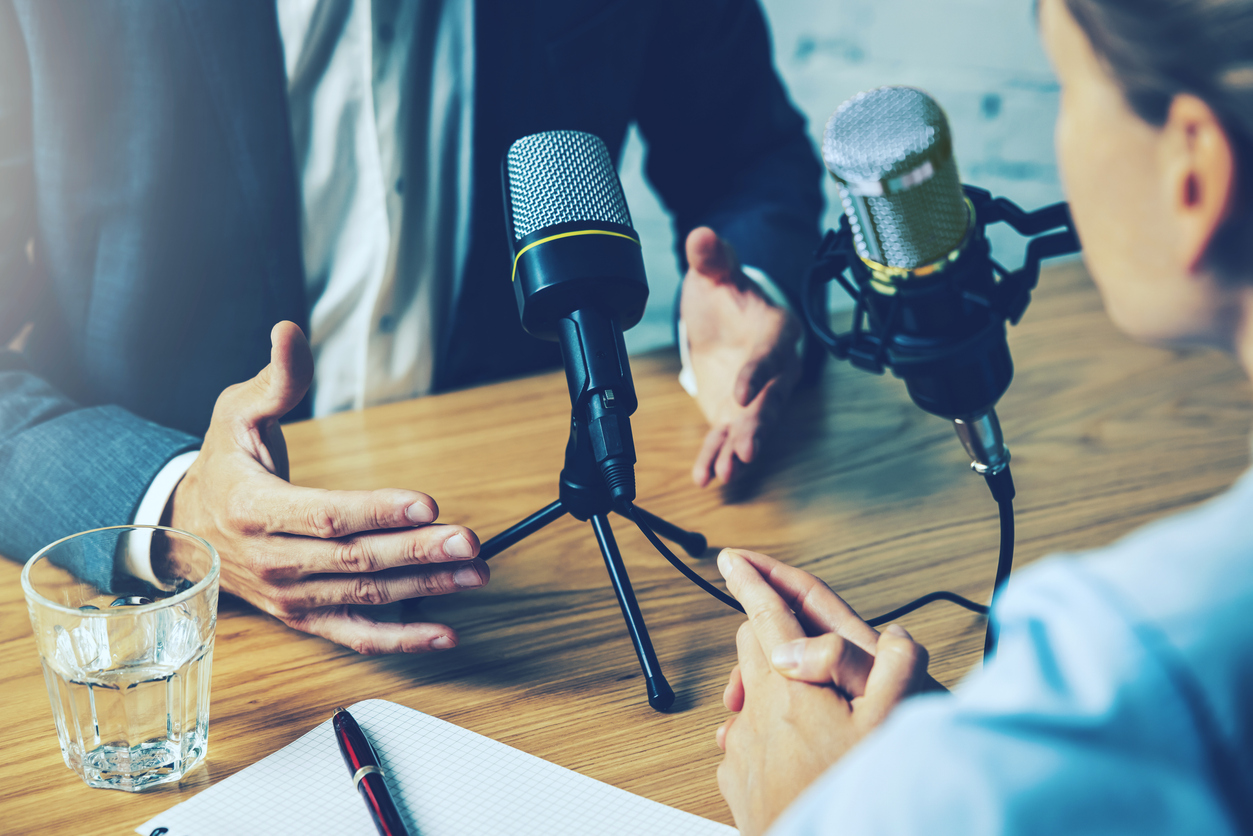 A man and woman seated at a table with microphones, engaged in a discussion for a CIO podcast